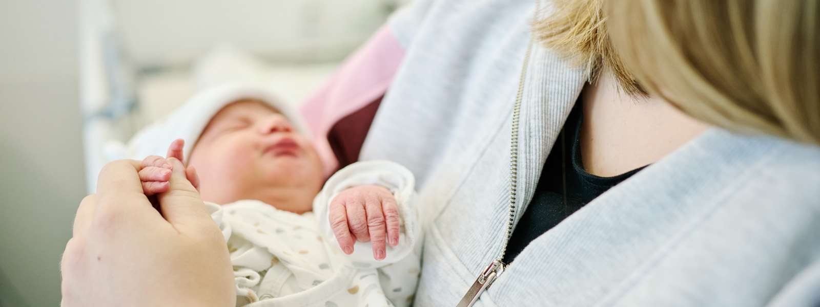 Mama im Patientenbett mit Neugeborenen unter dem Arm