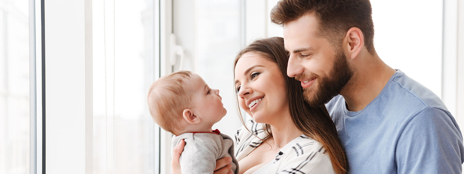 Familie bestehend aus Vater, Mutter und Baby steht glücklich zusammen am Fenster