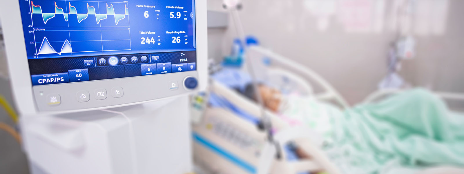 Monitor im Vordergrund, der Frequenzen misst, im Hintergrund (verschwommen) Intensivpatient:in